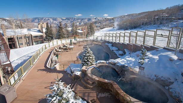 A snow-covered outdoor area with a hot tub, a snow-covered tree, and a view of mountains. - 🌲Timberline C1A Deluxe 3-Bedroom ~Hot Tub~Pool~WiFi~Ski-in/out~Local Shuttle🌲 (Snowmass Village)