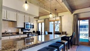 A modern kitchen with granite countertops, white cabinets, a large island with bar stools, and a dining area with a view of the outdoors. - 🌲Timberline C1A Deluxe 3-Bedroom ~Hot Tub~Pool~WiFi~Ski-in/out~Local Shuttle🌲 (Snowmass Village)