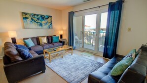 A living room with a sofa set, a coffee table, and a view through a glass door to the outside. - Oceanfront 2-bedroom condo at North Topsail Beach, perfect for family getaways. (North Topsail Beach)