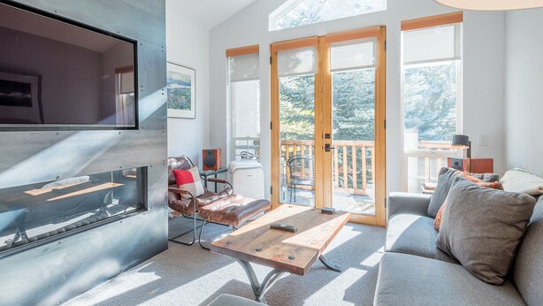 Un salon moderne avec une cheminée, un canapé, une table basse et une grande fenêtre donnant sur la forêt.