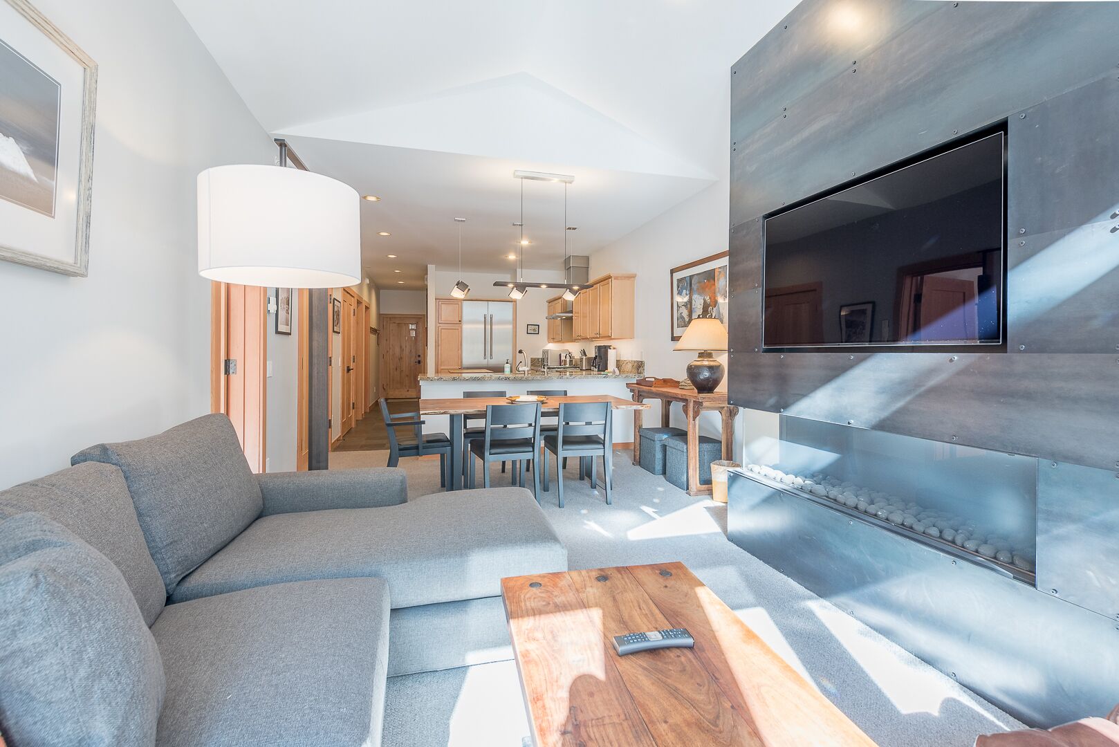Una sala de estar moderna con un sofá gris, una mesa de centro de madera y un televisor montado en una pared metálica.
