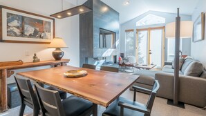 Un intérieur moderne avec une table à manger en bois, des chaises noires, un canapé et une grande fenêtre.