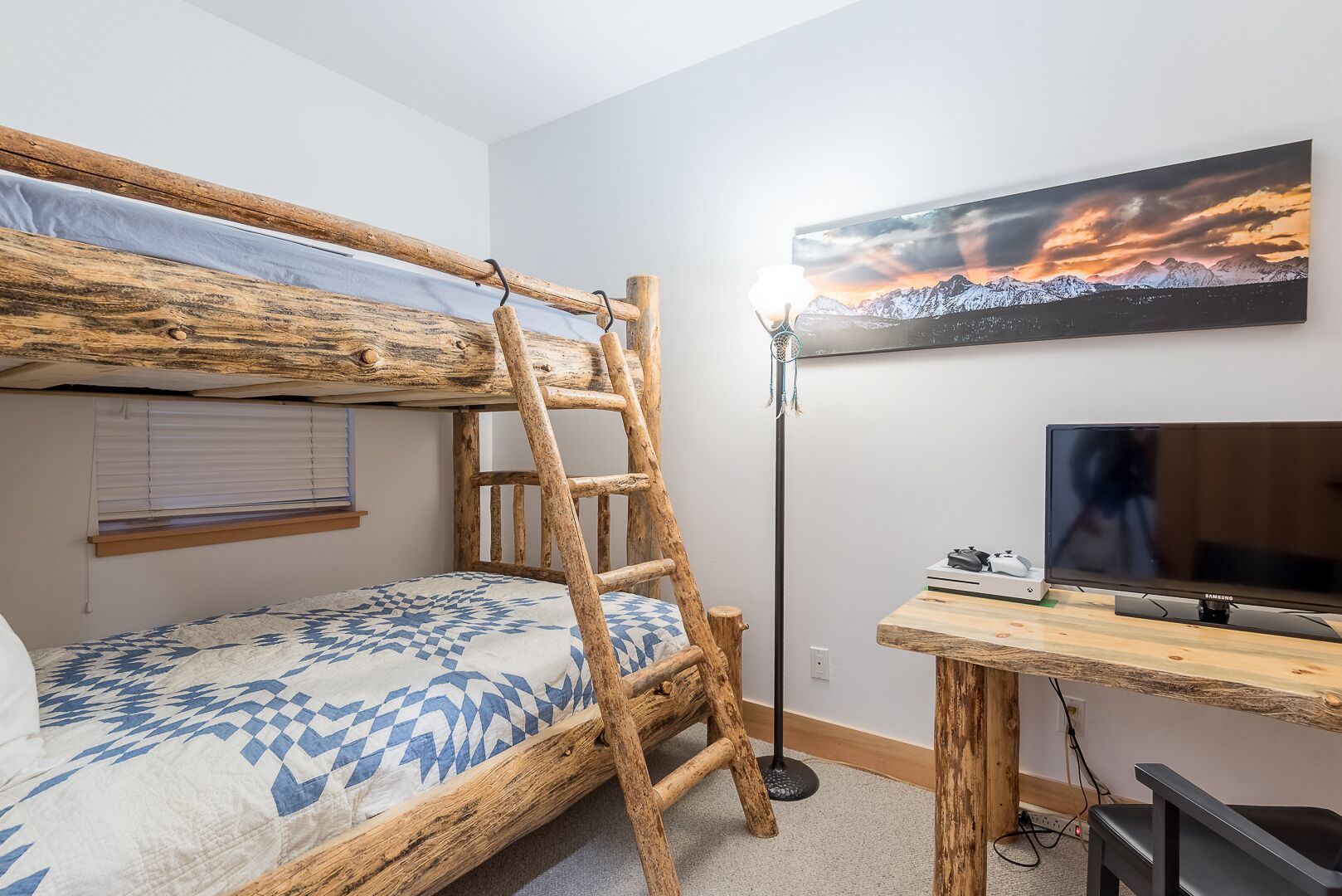 A bunk bed with a ladder, a desk with a computer, and a TV in a room with a mountain view.