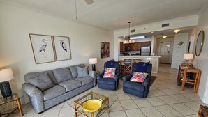 A living room with a grey sofa, two armchairs, a coffee table, and a dining area with a table and chairs. - The Inn at Dauphin Island 104 Walk right out to Pools and Beach! (Dauphin Island)