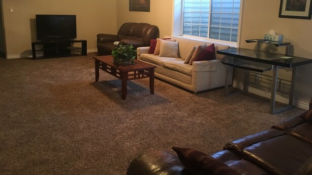 A living room with a brown leather couch, a beige sofa, a coffee table with a plant, a TV, and a window with blinds.