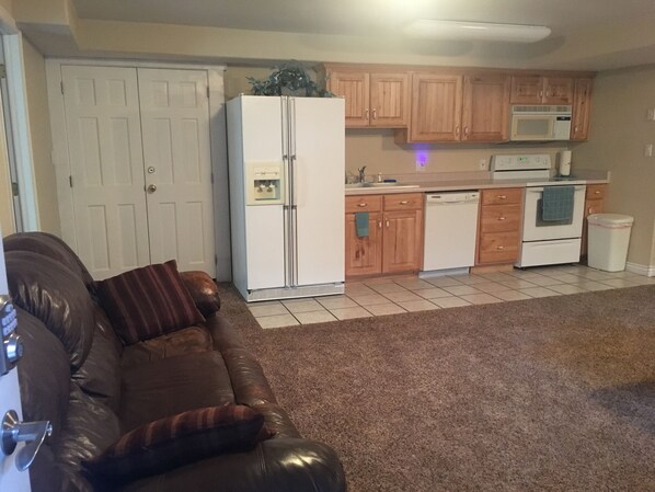 A compact living space with a kitchenette, a brown leather sofa, and a white refrigerator.