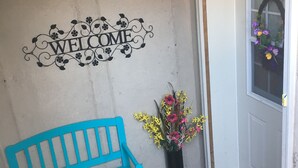 A blue bench, a welcome sign, a potted plant, and a door with a doormat.