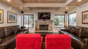 A cozy living room with a stone fireplace, leather sofas, and large windows offering a view of the outdoors. - Sun Valley Village | Pool Access | Deck (Sun Valley)