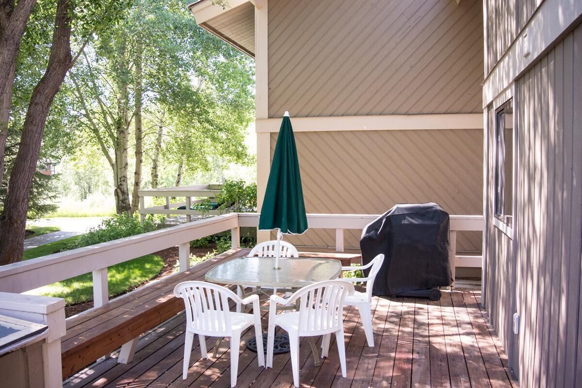 A covered outdoor patio with a round table and white chairs, a green umbrella, and a barbecue grill.