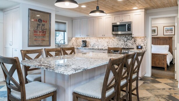 A kitchen with a large island, wooden chairs, white cabinets, and a microwave. - Sun Valley Village | Pool Access | Deck (Sun Valley)