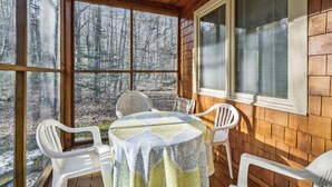 A covered porch with a table and chairs, large windows, and a view of a forest. - Glazebrook J5: 3-Bedroom Townhome with Sauna & Fireplace (Killington)