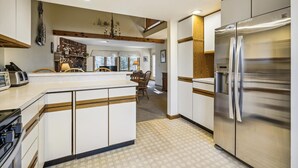 A modern kitchen with a central island, stainless steel appliances, and a dining area with a view. - Glazebrook J5: 3-Bedroom Townhome with Sauna & Fireplace (Killington)