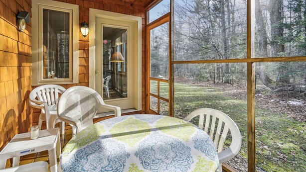A wooden cabin with a table and chairs, large windows, and a view of a forest. - Glazebrook J5: 3-Bedroom Townhome with Sauna & Fireplace (Killington)