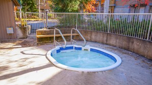 A small, round swimming pool with a metal ladder and steps, surrounded by a concrete deck and a metal fence.