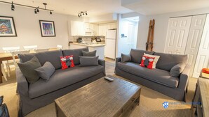 A modern living room with two grey sofas, a wooden coffee table, and a kitchen in the background.