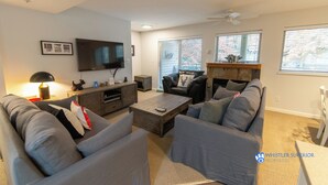 A modern living room with a flat-screen TV, grey sofas, a coffee table, and a fireplace.