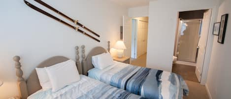 Habitación de hotel con dos camas, una mesita de noche, una lámpara y una puerta que da a un baño.