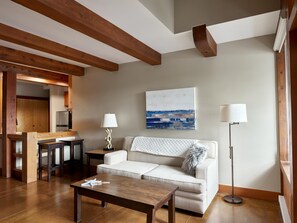 Een moderne woonkamer met een houten plafond, een witte bank, een salontafel, een lamp en een schilderij aan de muur.