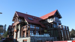 A multi-story building with a red roof and stone facade, featuring balconies and large windows. - Beautiful Condo in a Great Location, Oceanfront Complex - OE (Ucluelet)