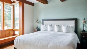 A bedroom with a large bed, wooden beams, a bench, and a view of the outdoors. - Beautiful Condo in a Great Location, Oceanfront Complex - OE (Ucluelet)