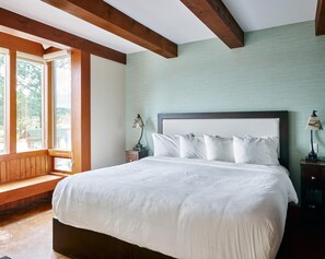 Een slaapkamer met een groot bed, houten balken, een bankje en uitzicht op het omliggende landschap.