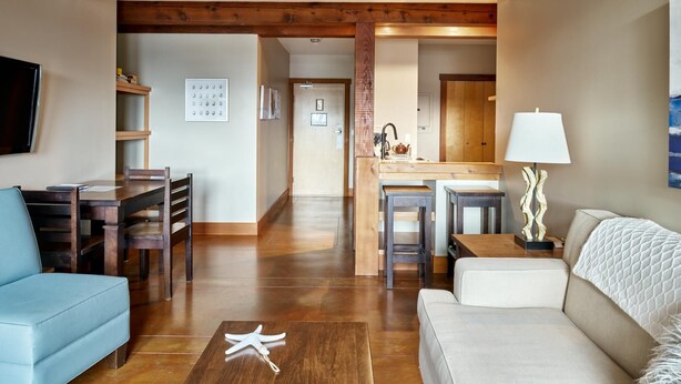A spacious living area with a wooden ceiling, a sofa, a coffee table, and a dining area with a kitchen in the background. - Beautiful Condo in a Great Location, Oceanfront Complex - OE (Ucluelet)