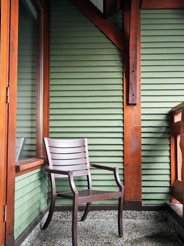 A wooden chair in a corner with a green exterior wall and wooden beams.