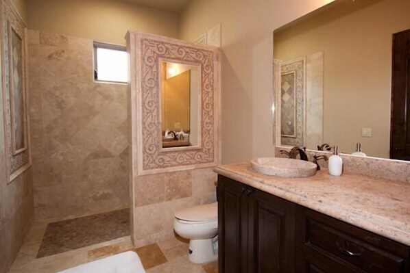 A bathroom with a marble sink, dark wooden cabinets, a white toilet, and a shower area with a decorative wall panel. - Pedregal Ocean View Luxury Villa, Walk to Marina, Resort Style Pool & Views !! (Caba San Lucas)