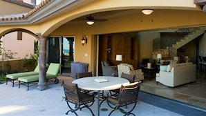 An outdoor patio with a round table and chairs, a covered seating area with a sofa, and a staircase leading to an upper level.