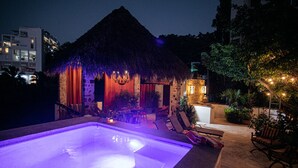 Een zwembadgedeelte met een rieten constructie, ligbedden en sfeerverlichting.