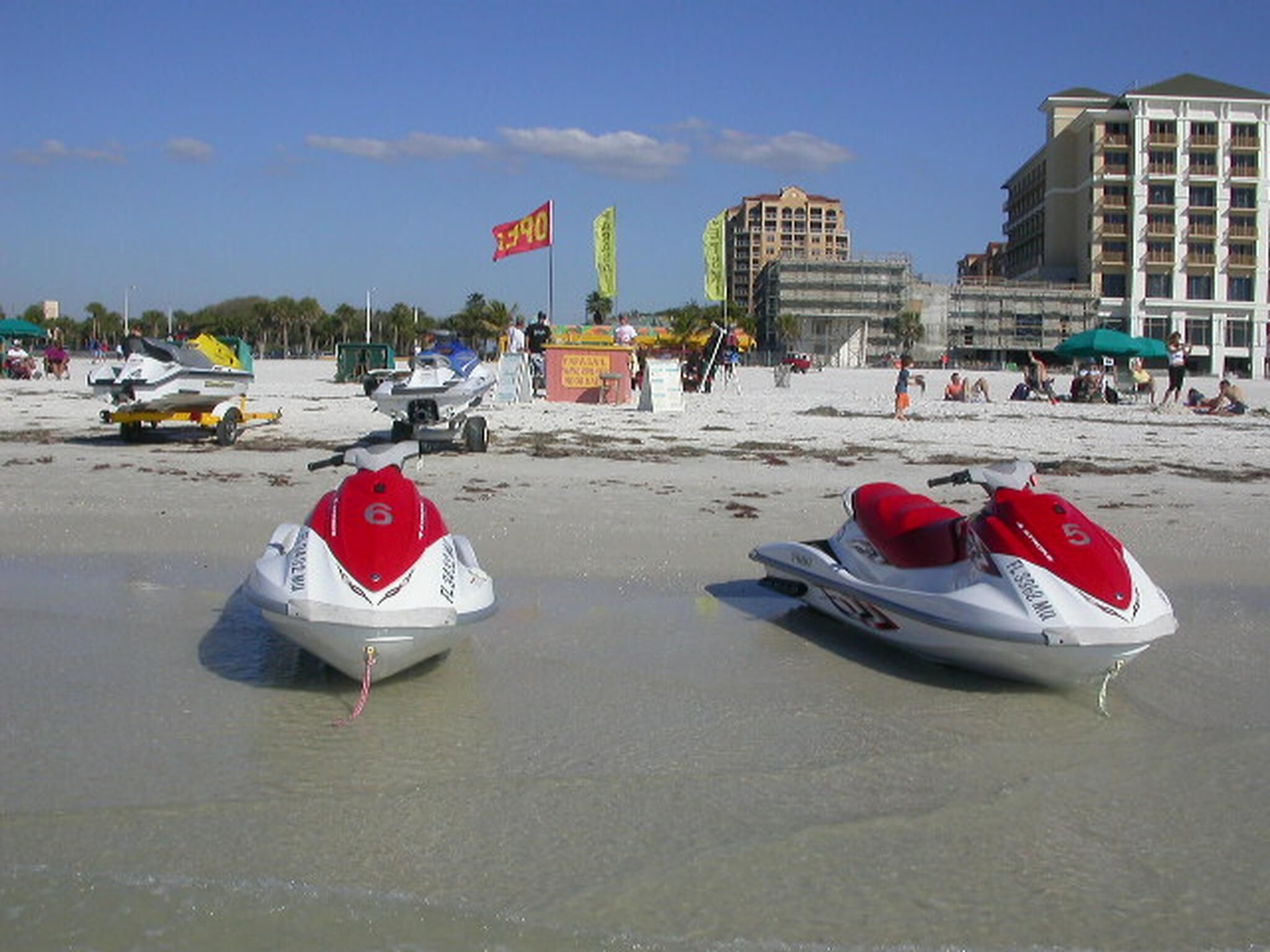 Jet skis on a sandy beach with buildings in the background.