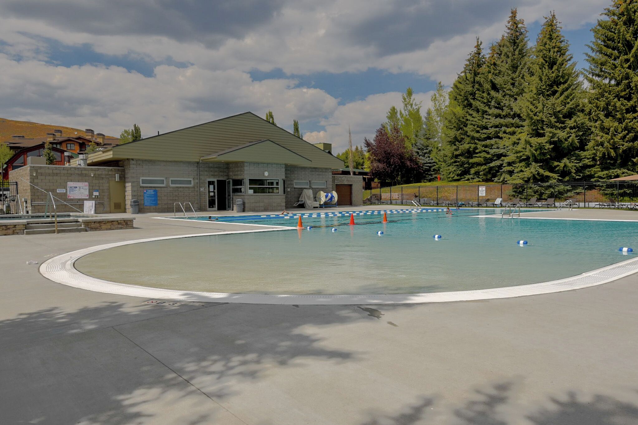Zona de piscina con un edificio, árboles y cielo despejado.