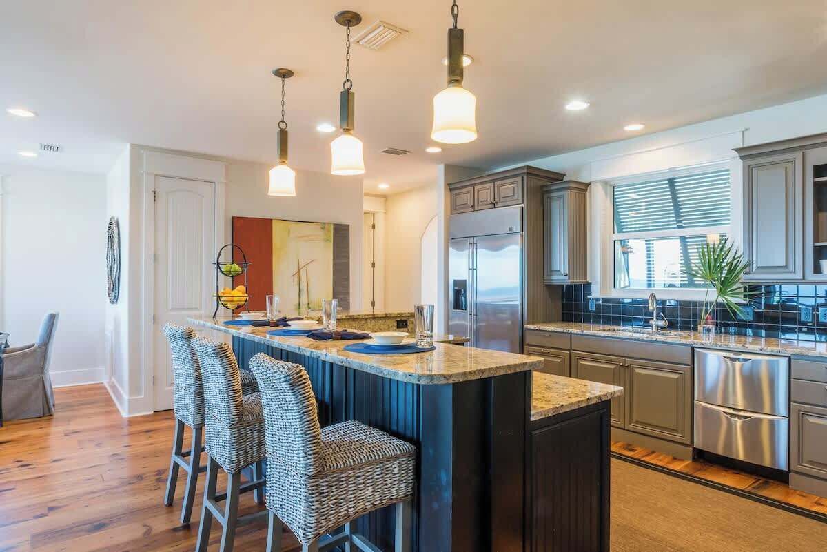 A modern kitchen with a central island, bar stools, stainless steel appliances, and pendant lighting.