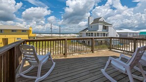 A wooden deck with two rocking chairs, a view of a beach, and a house with a white exterior and a chimney. - “Sea La Vie” Water Views,  Steps to the beach (Navarre Beach)