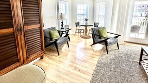 A spacious room with a wooden cabinet, a dining area with a round table and chairs, and large windows allowing natural light. - “Sea La Vie” Water Views,  Steps to the beach (Navarre Beach)