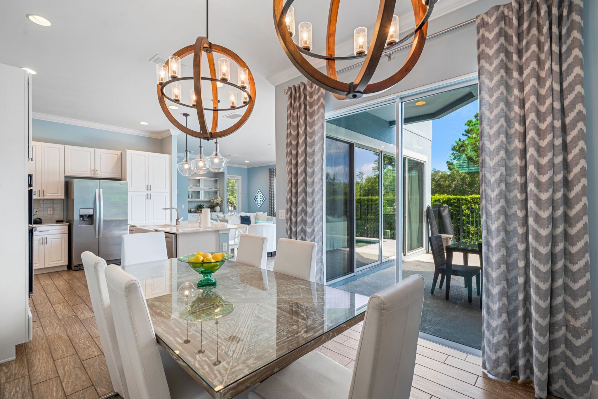 A modern kitchen with white cabinets, a stainless steel refrigerator, and a dining area with a glass table and white chairs.