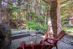 A covered patio area with stone pillars, a fire pit, and red chairs.