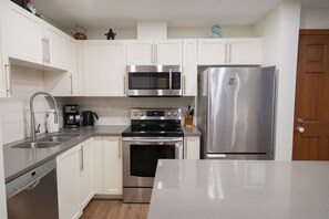 A modern kitchen with white cabinetry, stainless steel appliances including a microwave, oven, and refrigerator, a coffee maker, and a wooden door. - Stoney Creek Sunpath 8 (Whistler)
