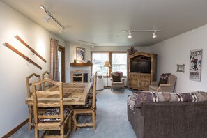 A cozy living room with a wooden dining table, two chairs, a sofa, and a television.