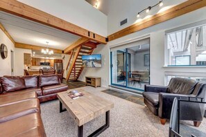 A spacious living area with a wooden ceiling, leather sofas, a coffee table, and a staircase leading to a kitchen.