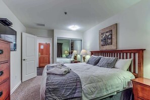 Un dormitorio con cama, mesitas de noche, armario, puerta y espejo.