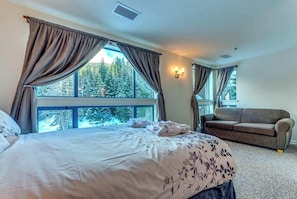 Ein Schlafzimmer mit Bett, einer Couch und großen Fenstern mit Vorhängen.