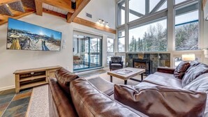 A spacious living room with a large window, a fireplace, and a leather sofa. - Greystone Lodge 413 Ski-in/Out by Acer Vacations (Whistler)