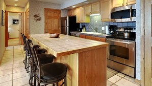 Una cocina moderna con una isla grande, taburetes de bar, electrodomésticos de acero inoxidable y armarios de madera.