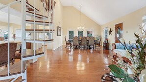 Un vaste espace de vie doté d’un haut plafond, d’un plancher en bois, d’une table à manger avec des chaises et d’un escalier muni d’une rampe.
