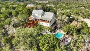 Une grande maison avec une piscine, entourée d’une végétation luxuriante et avec des collines en arrière-plan.