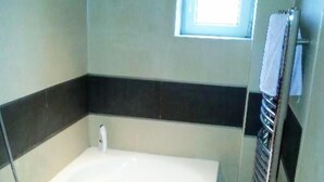 Ein Badezimmer mit einer großen Badewanne, einem kleinen Fenster und einem Handtuchhalter.