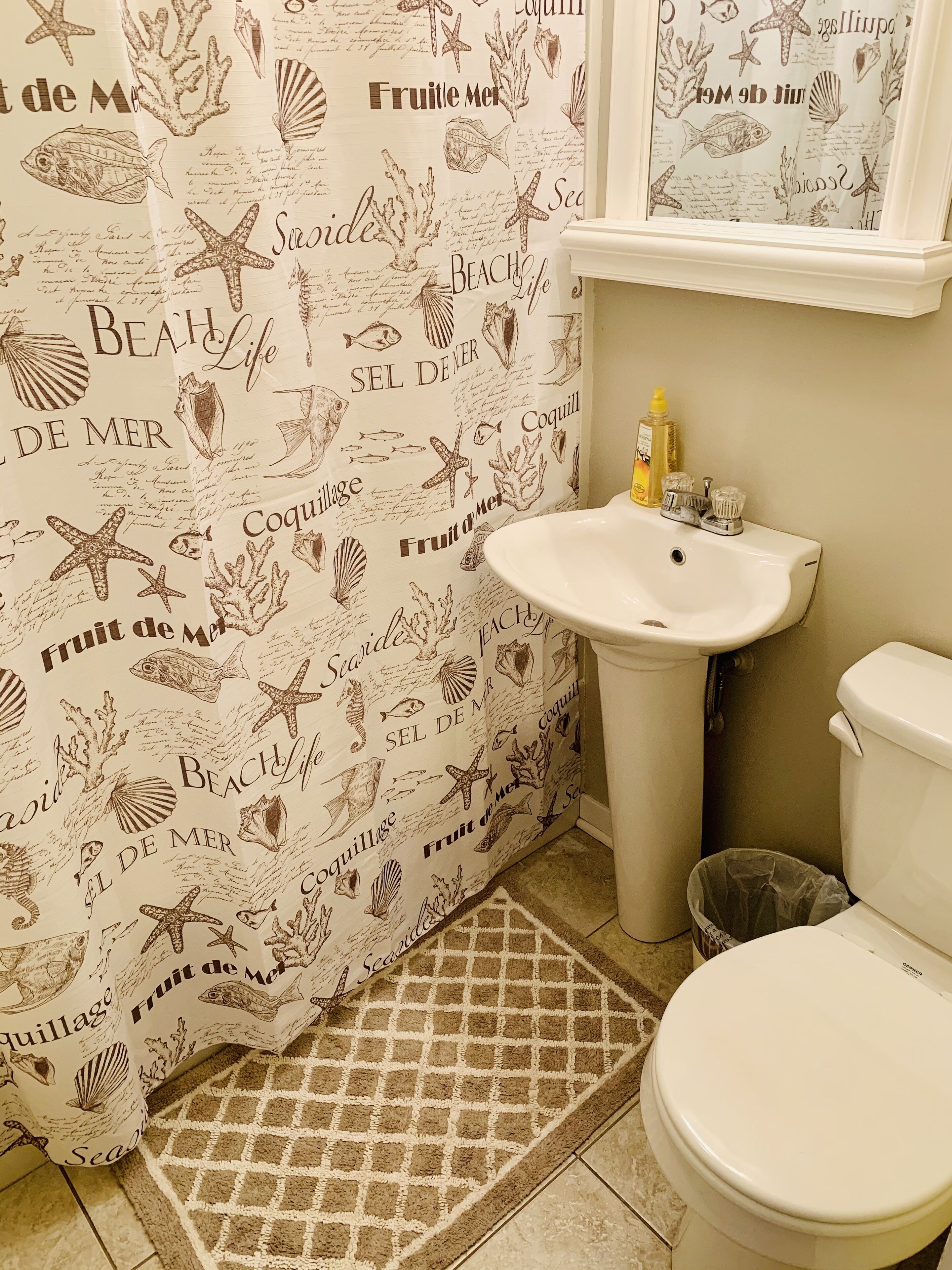 Un baño con cortina de ducha de temática marina, un lavabo y un inodoro.
