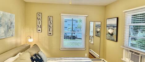 A bedroom with a bed, a ceiling fan, a window with blinds, and wall decorations including signs and artwork.