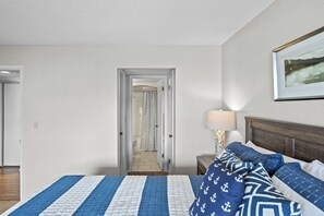 Habitación de hotel con cama, mesita de noche, lámpara, un cuadro enmarcado en la pared y un baño visible a través de una puerta abierta.